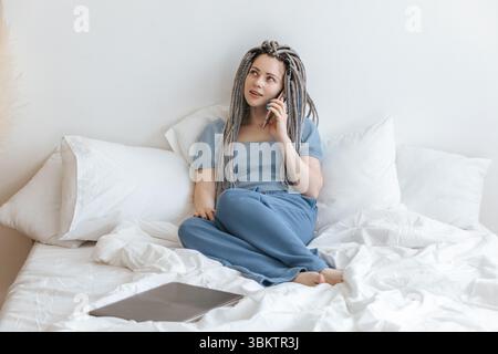 Young woman talking on the phone in white bed. Stock Photo