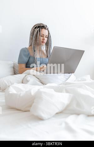 Business woman working on laptop in white bed. Stock Photo
