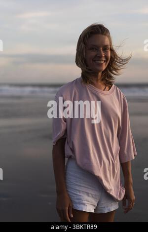 Smiling woman standing on a breezy beach during sunset Stock Photo