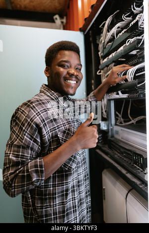 Technician organizes network equipment while smiling in data center during afternoon hours Stock Photo