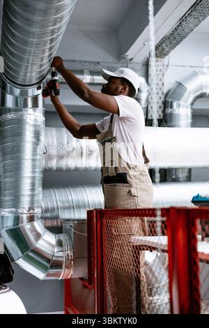 Skilled worker installing ventilation pipes in modern facility during daylight hours Stock Photo