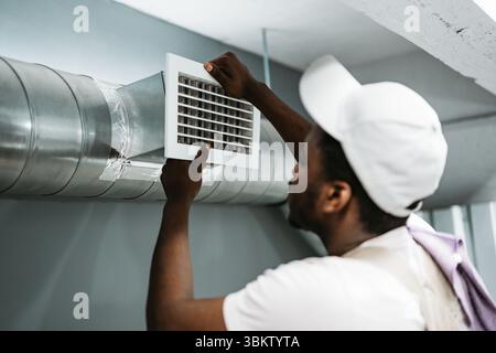 Worker installing air duct vent in a residential basement during the day Stock Photo