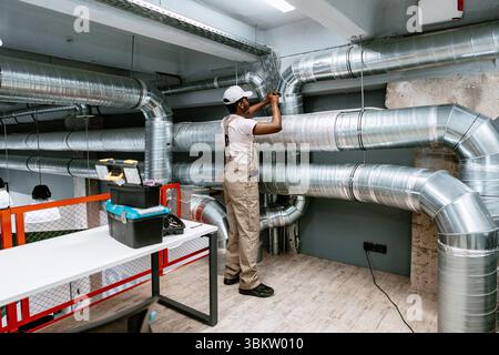 Skilled worker installing ventilation system in modern commercial building during daytime Stock Photo