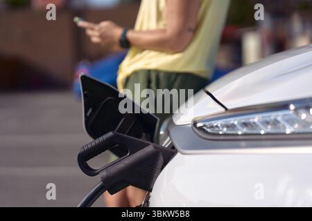 Driver charging electric car at station using mobile phone app - sustainability and clean energy concept Stock Photo