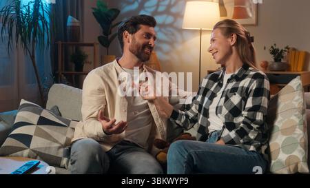 Caucasian joyful man with woman couple married female male talking relaxed on sofa in living room at evening resting couch happy family communication Stock Photo