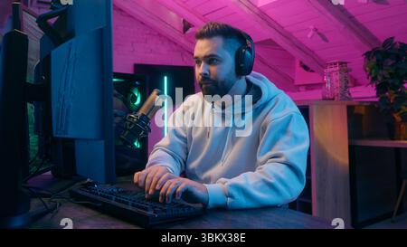 Concentrated guy male gamer streamer man wearing headphones gaming at computer focused streaming in neon light room indoors online match modern Stock Photo