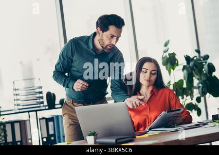 Two coworkers engaged in a focused discussion at a modern office desk, collaborating over digital and printed materials Stock Photo