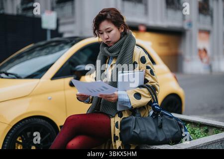 Young woman analyzing documents outdoors next to a yellow car Stock Photo