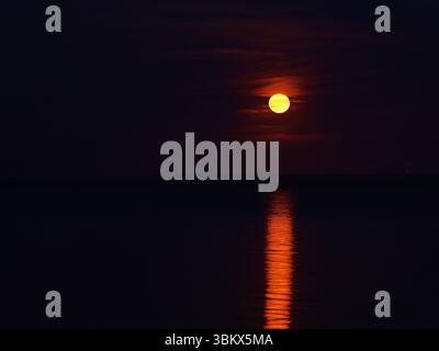 Red strawberry moon rises over the Greifswalder Bodden in June 2025. Mystical glow reflects on the water. Copy space, Space for  texts and desings. Stock Photo