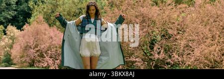 Curly-haired woman showcases a trendy raincoat while enjoying the outdoors in summer, banner Stock Photo