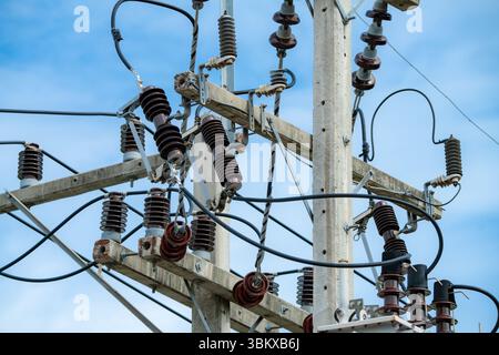 Close-up view of high voltage electrical transmission equipment on concrete utility pole with insulators and cables under blue sky showcasing modern Stock Photo