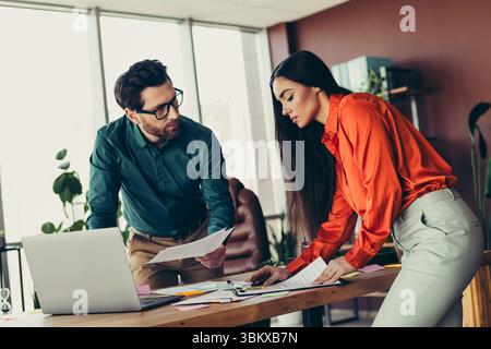 Two focused professionals collaborate on a business project in a modern workspace, discussing documents and strategies for success Stock Photo