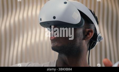 3d world gaming African American man male guy using controllers VR helmet virtual augmented reality glasses high-tech Internet technology futurism Stock Photo