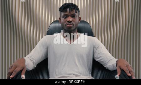 Futuristic confident serious gamer programmer hacker African American man guy male sitting in chair in futurism modern room studio in chair looking at Stock Photo