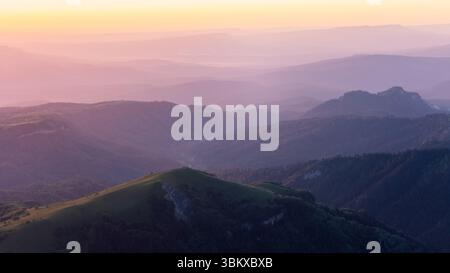 Peaceful mountain landscape at sunrise with colorful misty layers and soft golden light. Stock Photo