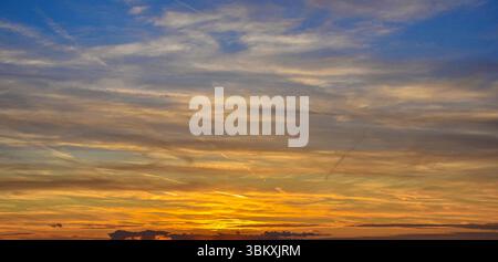 Serene sky during sunset, featuring layered clouds lit in orange, yellow, and blue-gray, evoking warmth and tranquility. Stock Photo