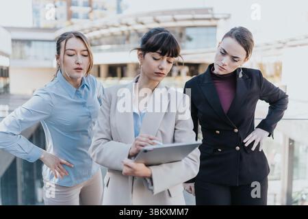 Three female professionals collaborating on a project using a tablet outdoors Stock Photo