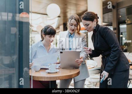 Three businesswomen collaborating on a tablet during a casual meeting in a modern cafe Stock Photo