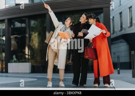 Three female professionals discuss plans outdoors with documents Stock Photo