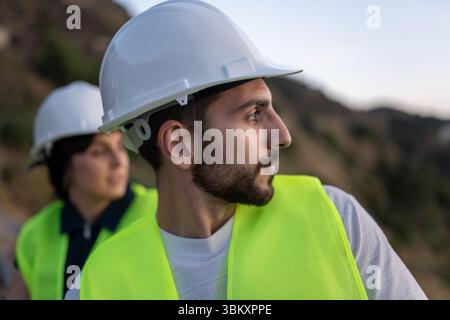 Young adult engineers wearing safety helmets inspecting construction site Stock Photo