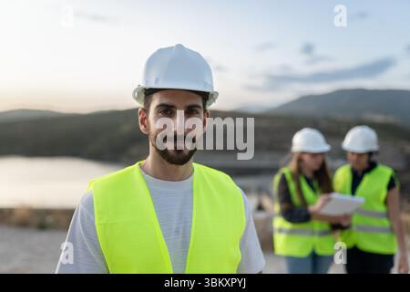 Young male engineer smiling at camera with colleagues working in background Stock Photo