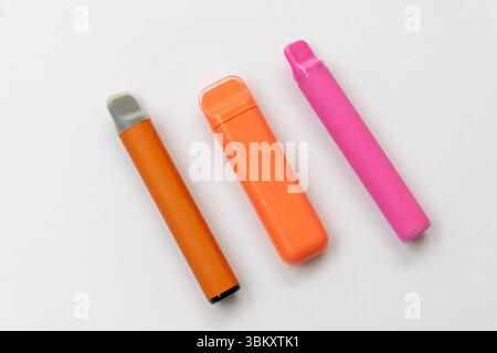 Three disposable electronic cigarettes in bright colors on a white background. Modern vape devices lying in a row Stock Photo