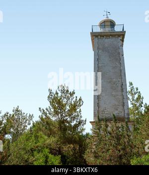 The Victorian lighthouse seen above the forest canopy against the pale blue sky, Fiscardo, Kefalonia, Greece Stock Photo