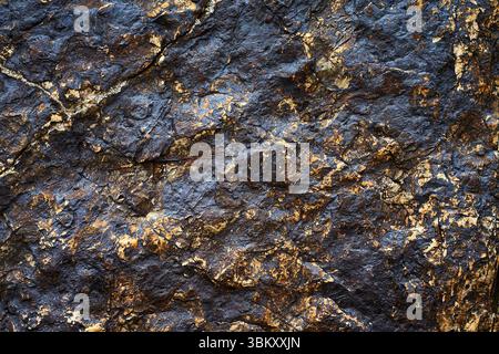 Close-up of textured rock surface with gold and brown hues. Chimgan Mountains, Uzbekistan. June 2025 Stock Photo