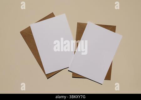 Two blank white cards placed on brown kraft envelopes over neutral beige table background. Minimalist flat lay. Birthday invitation, greeting card Stock Photo