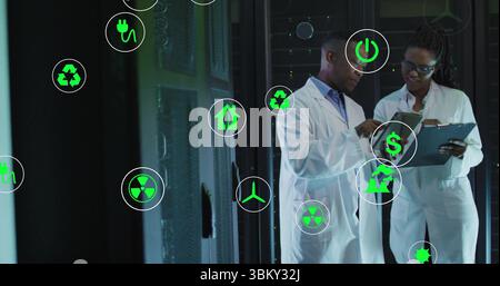 Holding clipboard, researchers in lab coats analyzing energy data at server racks with energy icons Stock Photo