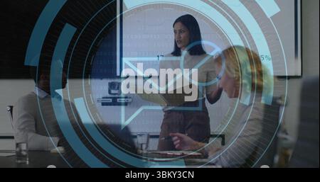 Presenting woman in blouse and skirt discussing report at conference table, with folder and screen Stock Photo