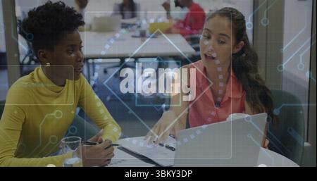 Collaborating two women discussing documents on laptop in office meeting room, with 6G overlay Stock Photo