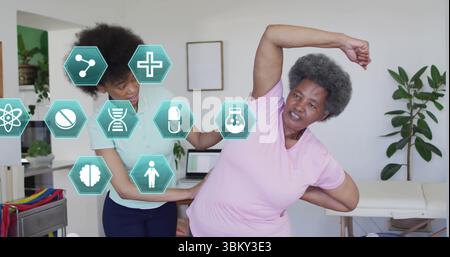 Assisting client doing side stretch in therapy room with cart laptop interface icons, copy space Stock Photo