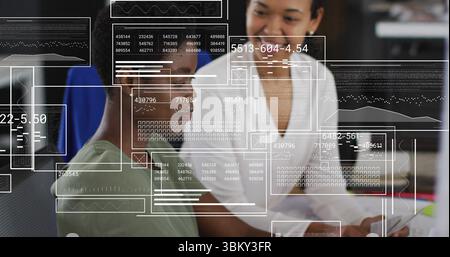 Collaborating colleagues in green and white tops analyzing computer data in office with data panels Stock Photo