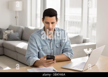 Focused young male remote working professional multitasking using phone notebook Stock Photo
