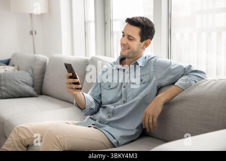 Happy young man spend time relaxing on sofa with phone Stock Photo