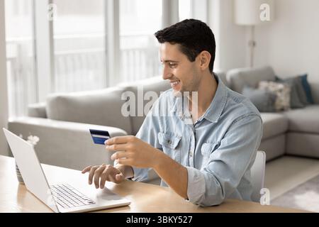 Smiling young man pay online from credit card using notebook Stock Photo