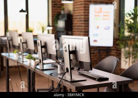 Vacant and organized brick wall office featuring a table and digital equipment for startup company. Empty modern workspace that is well arranged with multiple computers, ready for employees. Stock Photo