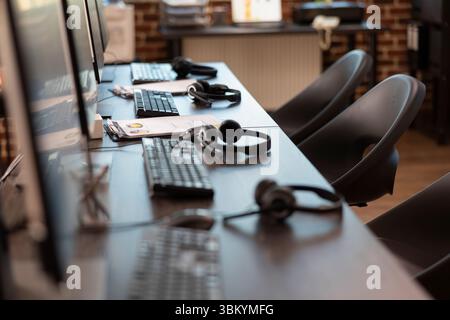 Empty office with sleek workstation, emphasizing a ready environment for company research and analysis. The vacant table is neatly arranged with headsets and clipboards for group of employees. Stock Photo