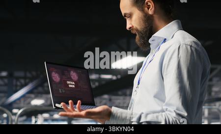Annoyed engineer in data center reacting to critical error message on laptop. Irked IT professional attempts to resolve system fault impacting backend infrastructure performance Stock Photo