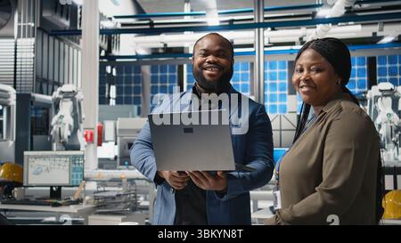 Black factory inspectors engaging in a briefing over the manufacturing process, reviewing production line and metrics on files. Supporting renewable energy improvement. Camera A. Stock Photo