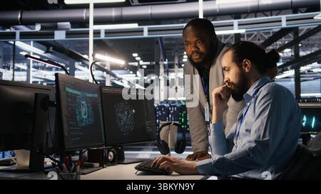 Supervisor in server room monitoring worker managing AI training datasets. African american team leader and engineer in data center supervising system operations supporting neural networks, camera A Stock Photo