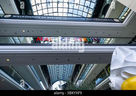 Indoor view of the Mall of Berlin with colorful rainbow sign, welcome banner, and modern glass roof above shopping levels. Stock Photo