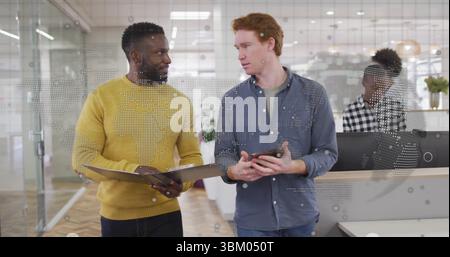 Discussing coworkers holding ring binder and tablet in modern open-plan office, with reception desk Stock Photo
