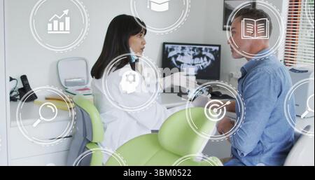 Dentist in lab coat and gloves consulting patient in clinic, with digital icons and X-ray monitor Stock Photo