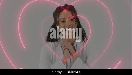 Smiling woman wearing white lab coat standing in professional studio, with neon pink heart graphics Stock Photo