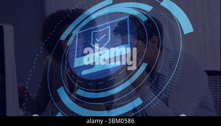 Reviewing cybersecurity overlay specialist and analyst in blazer working at office desk shield icon Stock Photo