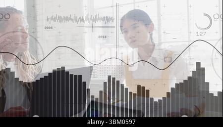 Analyzing digital bar and line charts, male and female professionals working in office, with laptop Stock Photo