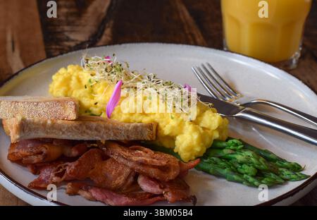 Breakfast plate with scrambled eggs, bacon, steamed asparagus and toasted bread Stock Photo