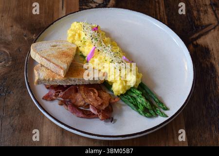 Breakfast plate with scrambled eggs, bacon, steamed asparagus and toasted bread on wooden table Stock Photo